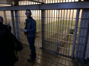 Jason standing in front of a cell, listening to the audio tour